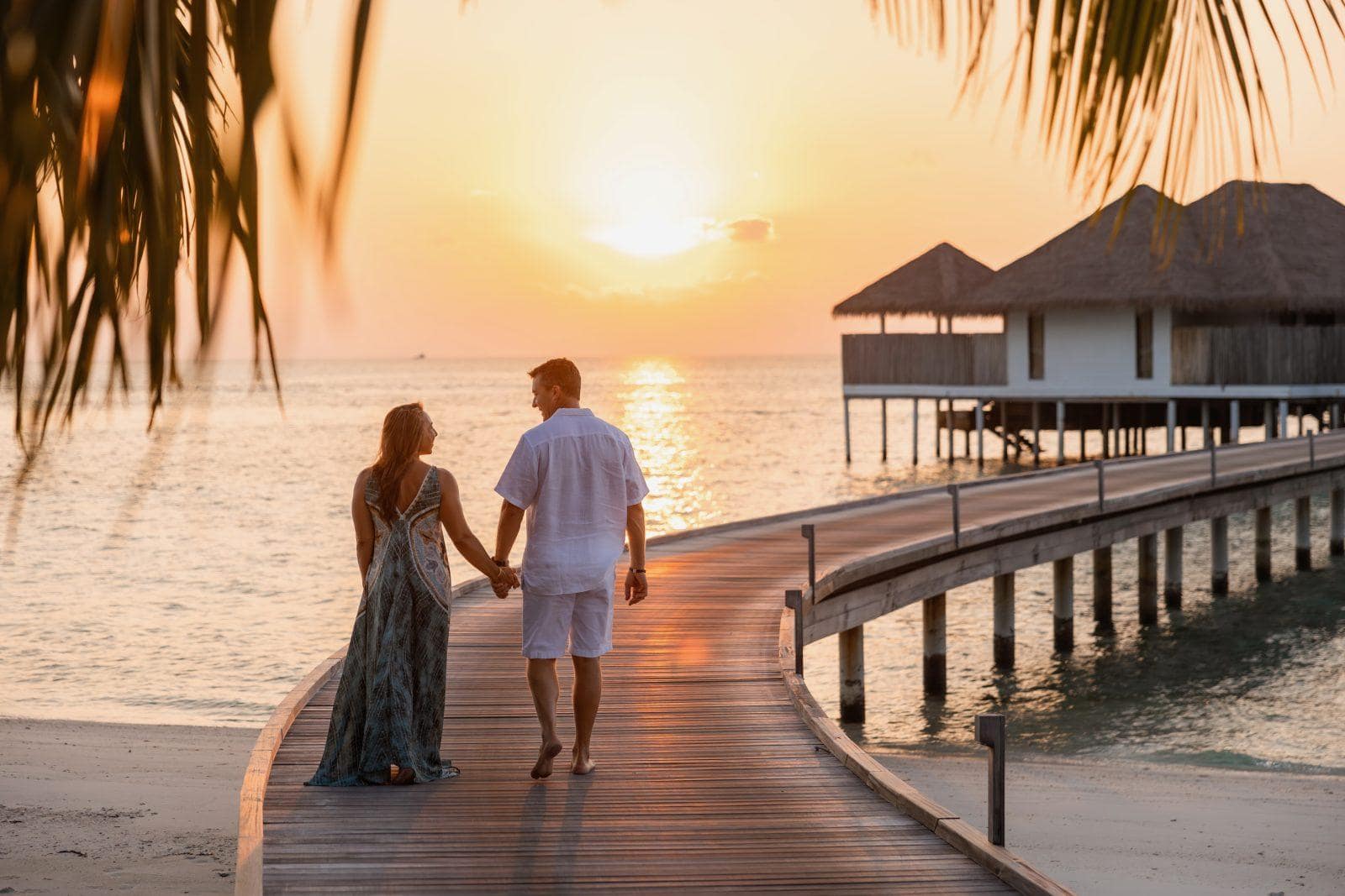 happy midlife couple walking into the sunset hand in hand at a resort in resort wear
